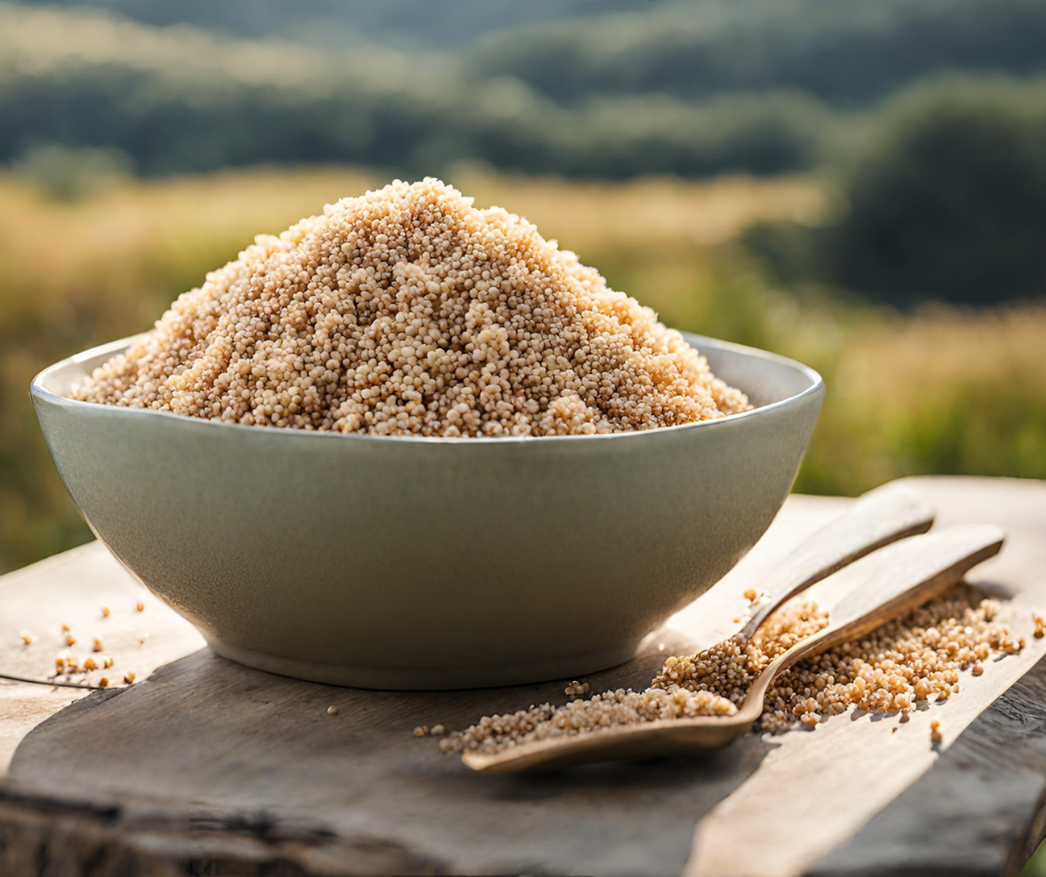 Miska plná quinoi na stole. V pozadí je výhľad na prírodu. VedĽa misky je drevená lyžica tiež plná quinoi. Na obrázku je biela quinoa. Zelený obchodík